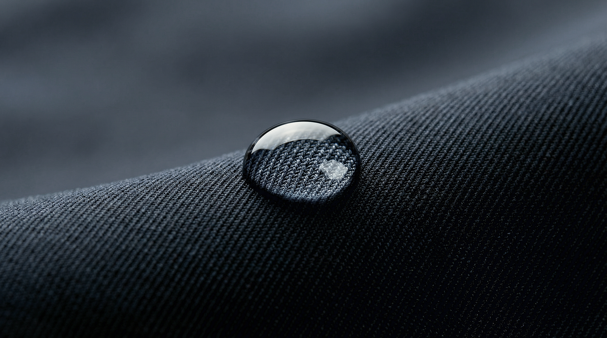 Macro d’une goutte d’eau reposant sur un textile technique bleu sans pénétration.