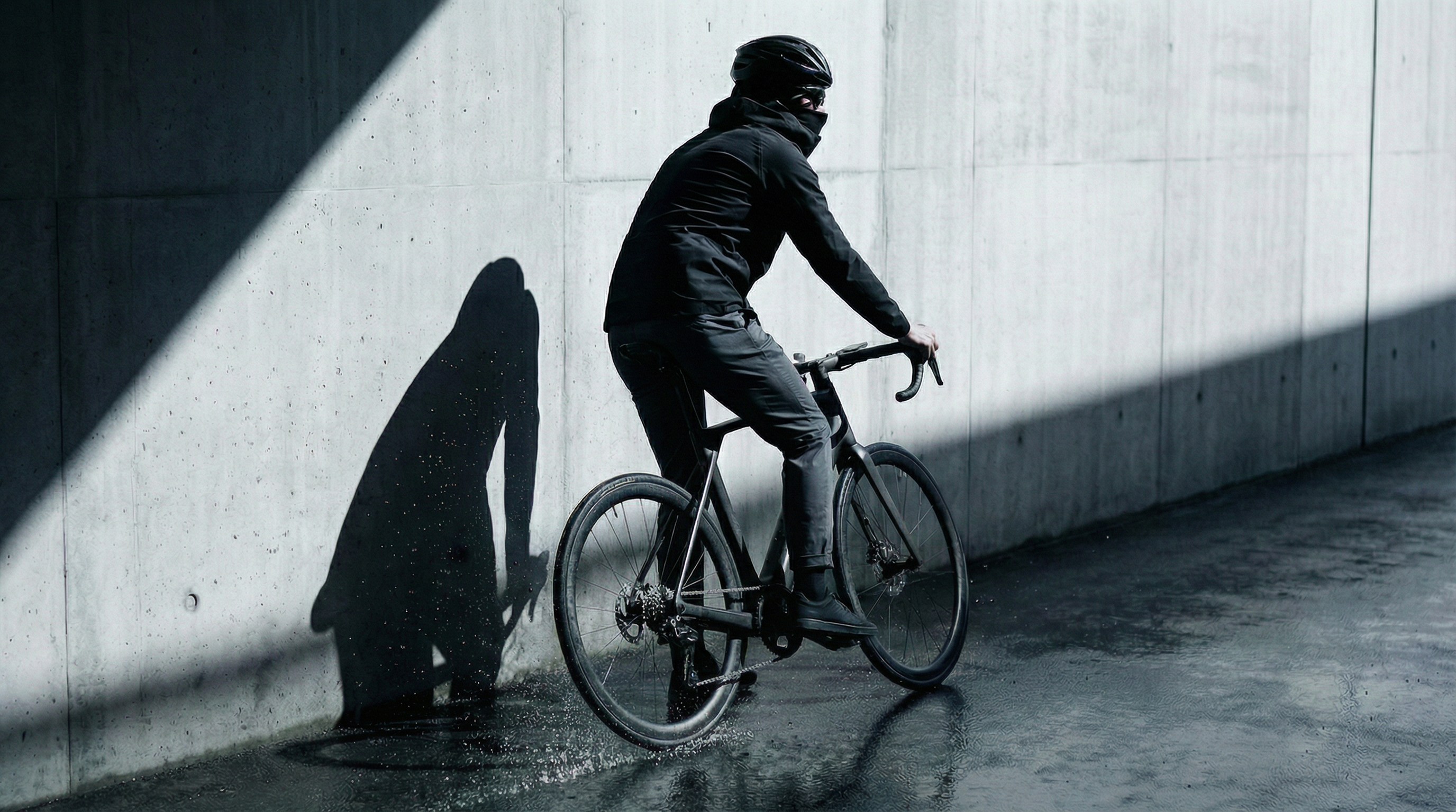 Veste Ultra Hardshell noir portée par un homme à vélo sous la pluie.
