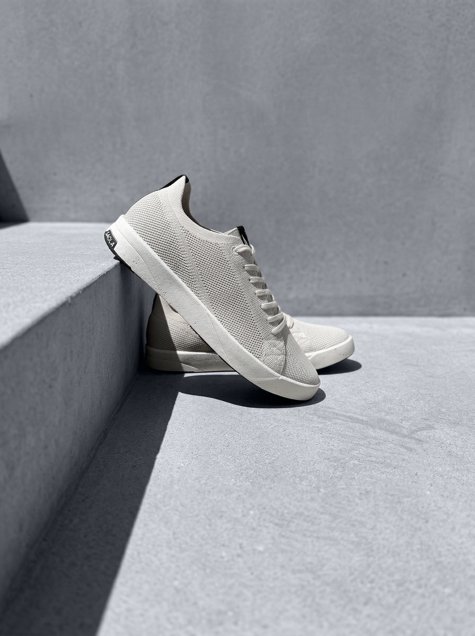 Chaussures beige épurées adossées à des marches minérales, jeu d’ombres graphiques.