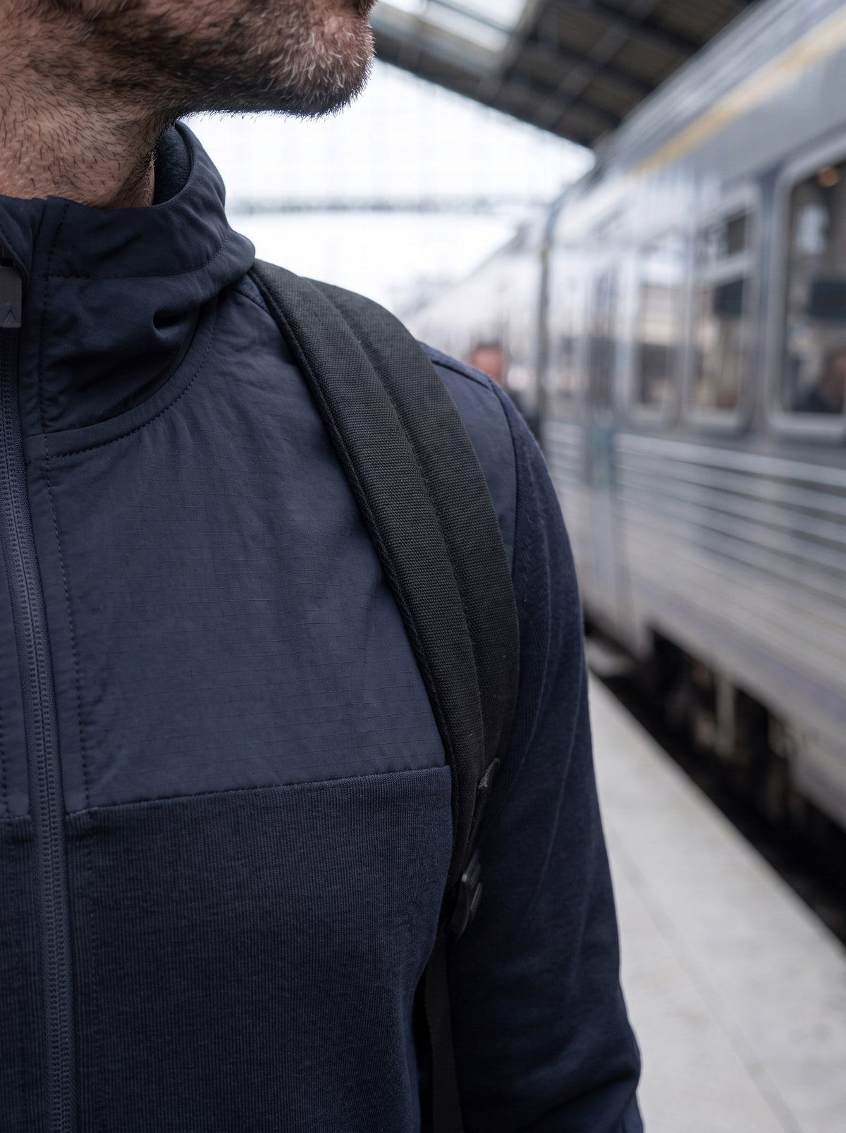 Bretelle de sac à dos sur l'épaule du 360 Merino Hoodie, sur un quai de gare