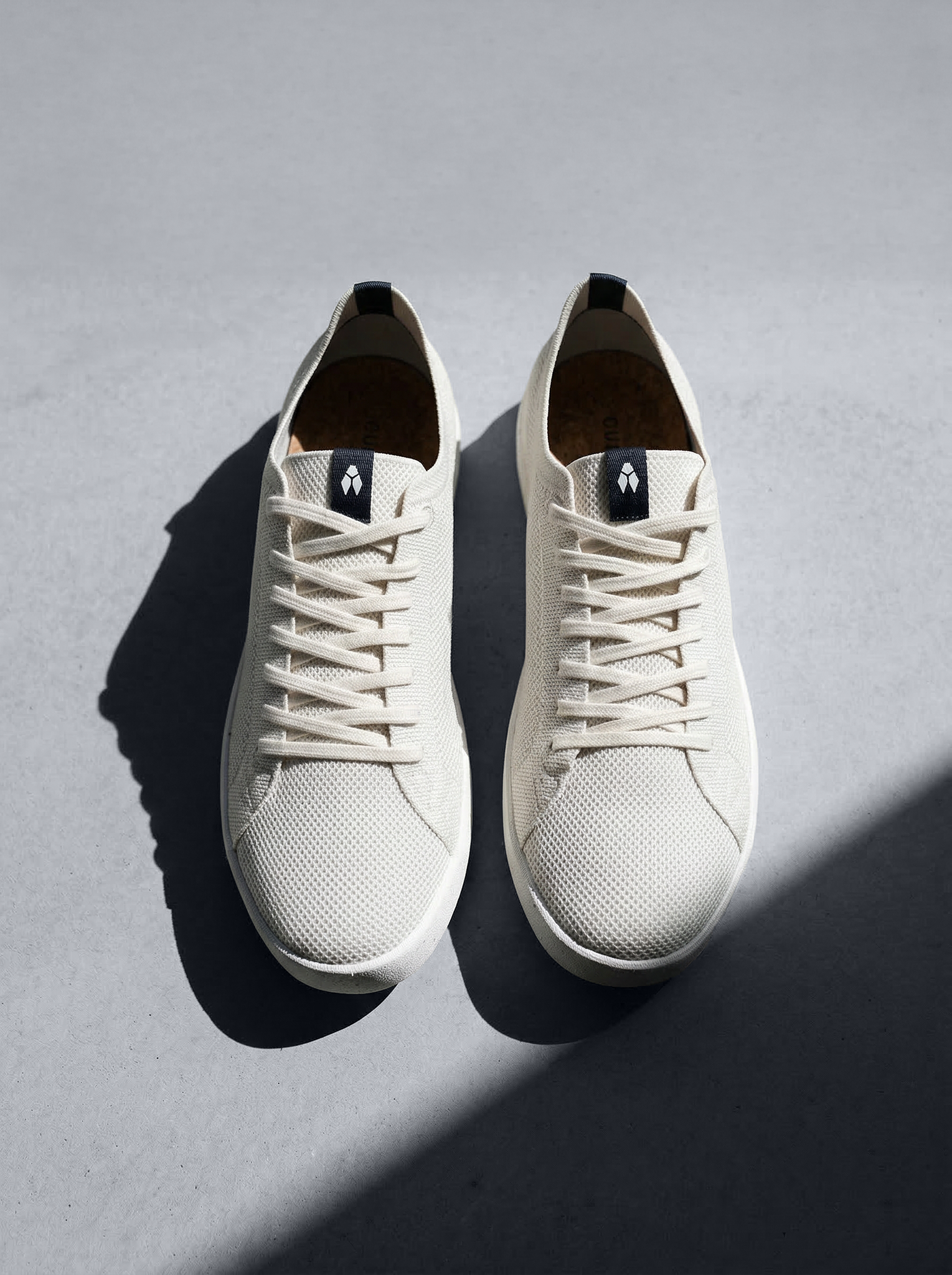 Baskets en maille respirante beige avec languette noire contrastée, composition symétrique.