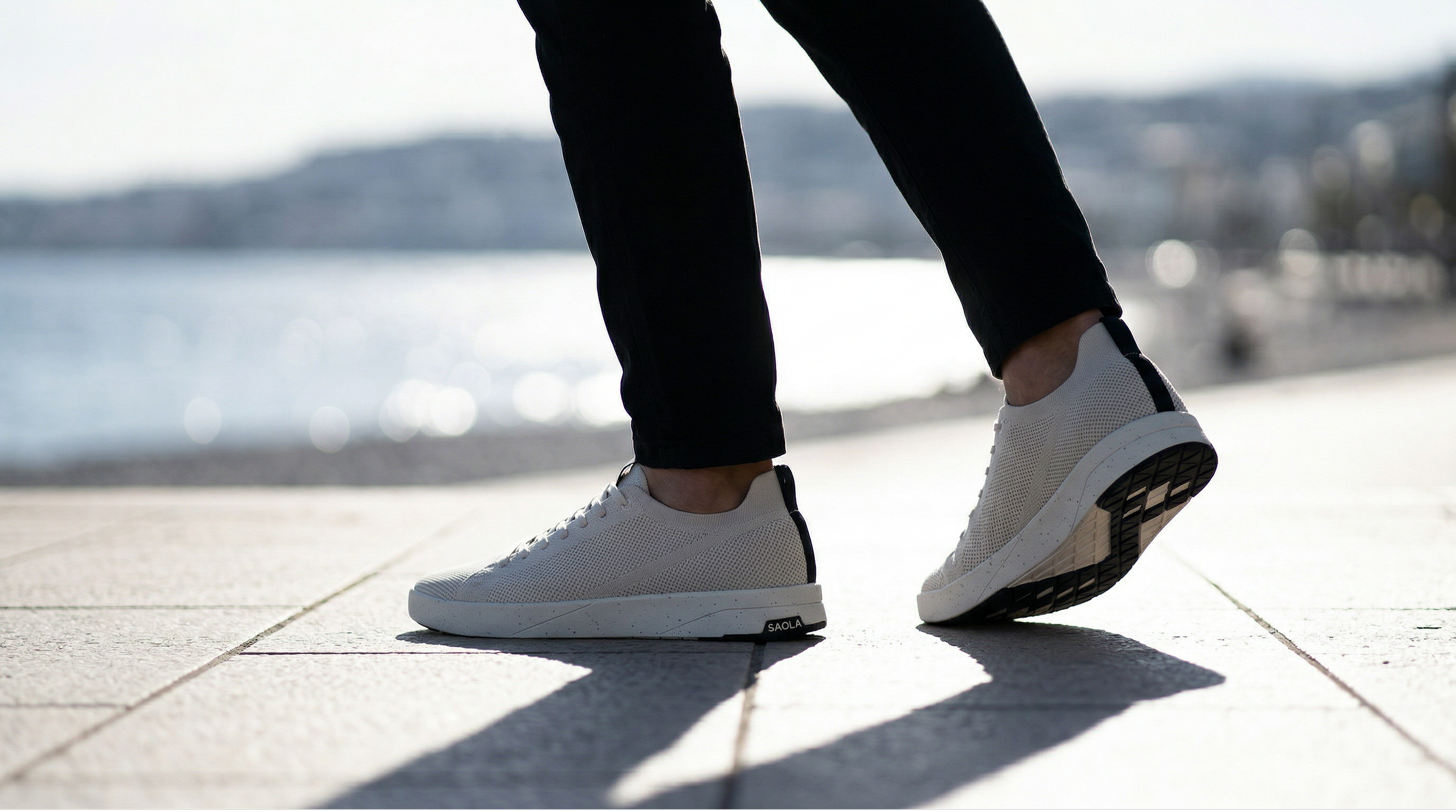 Sneakers blanches légères portées en bord de mer avec semelle contrastée noire.