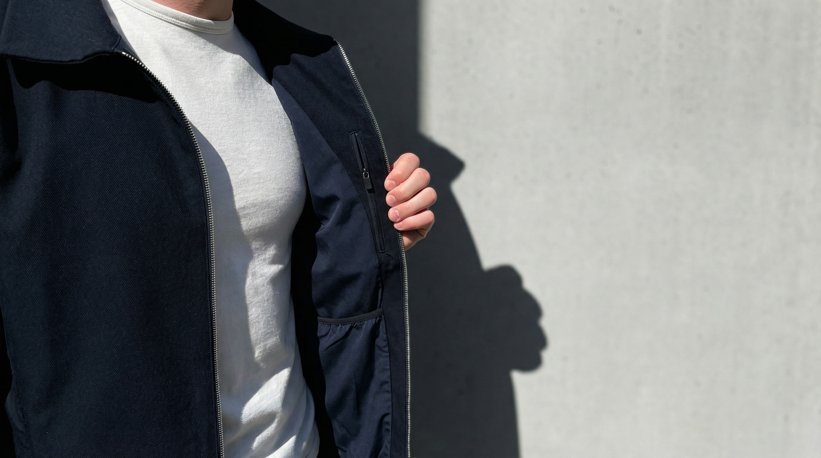 Gros plan sur doublure intérieure et poche zippée d’une veste bleu nuit minimaliste.