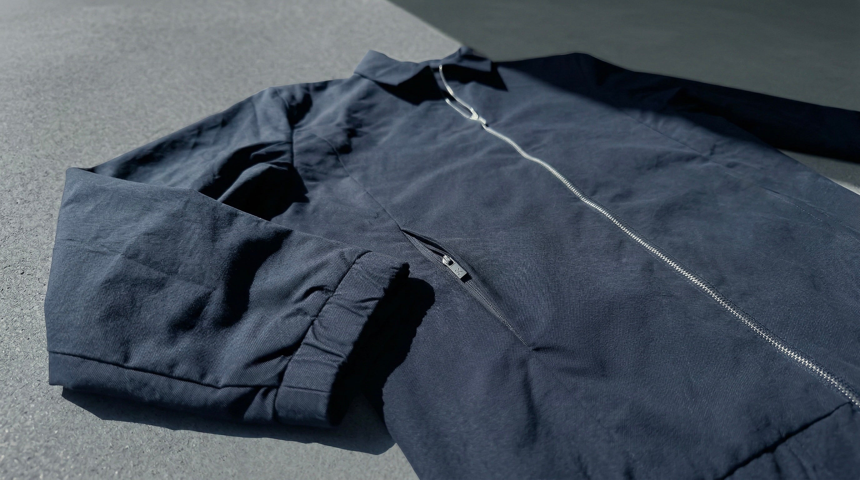Détail de veste bleu nuit avec fermeture éclair métallique et poche discrète intégrée.