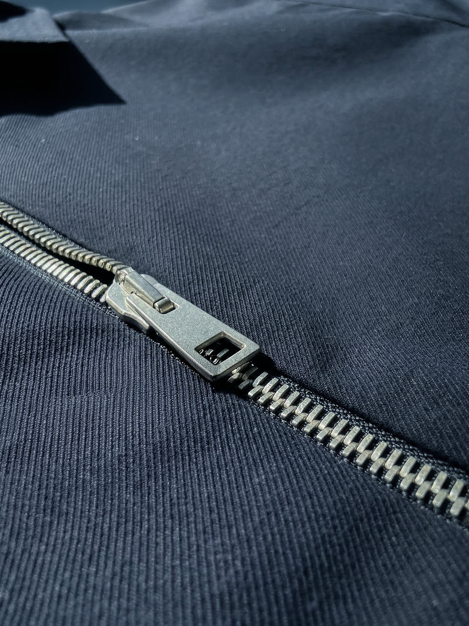Détail d’une veste bleu marine avec fermeture éclair centrale et poche poitrine discrète.