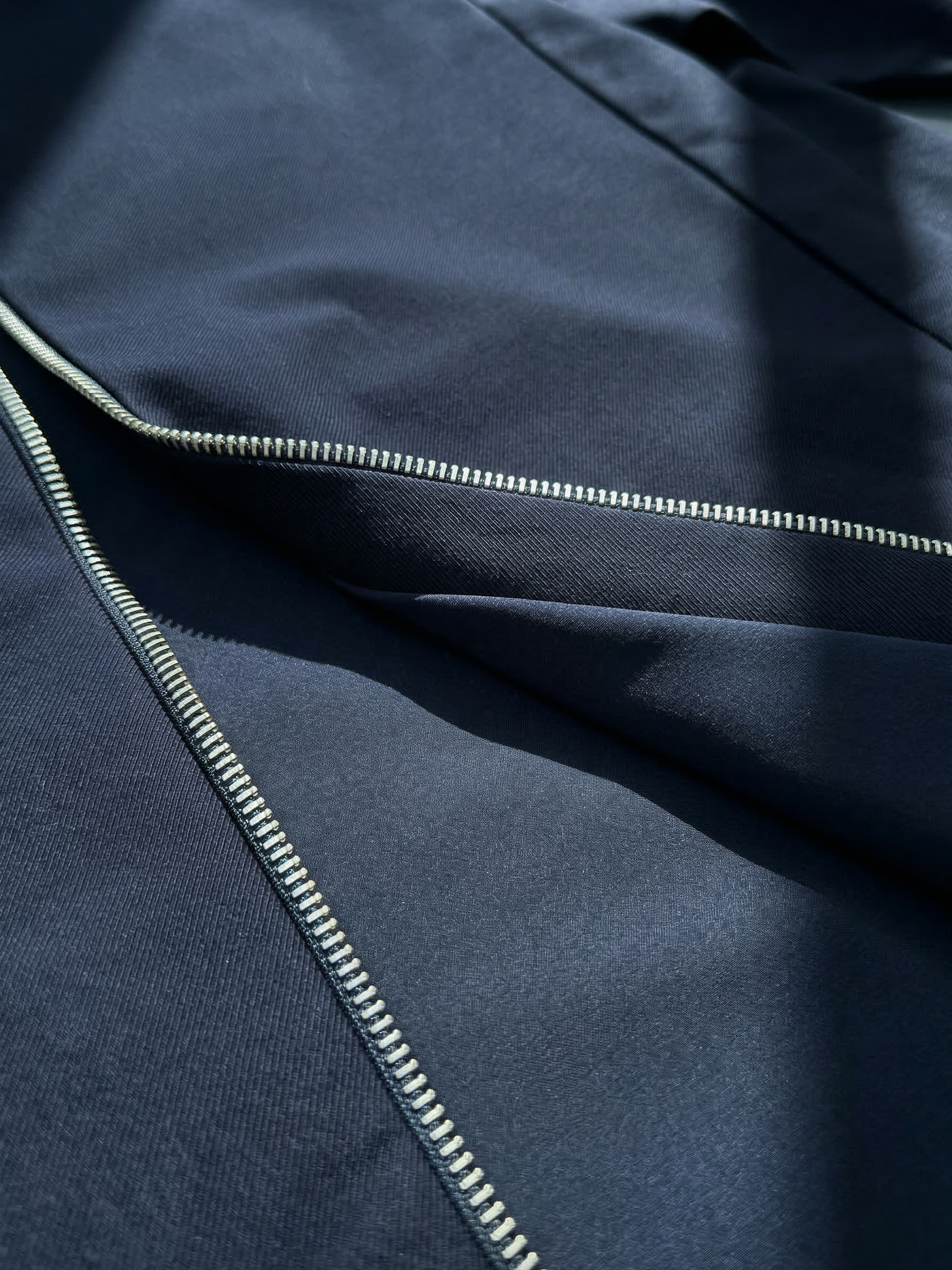 Gros plan sur la fermeture zippée argentée et la texture du tissu technique bleu marine.