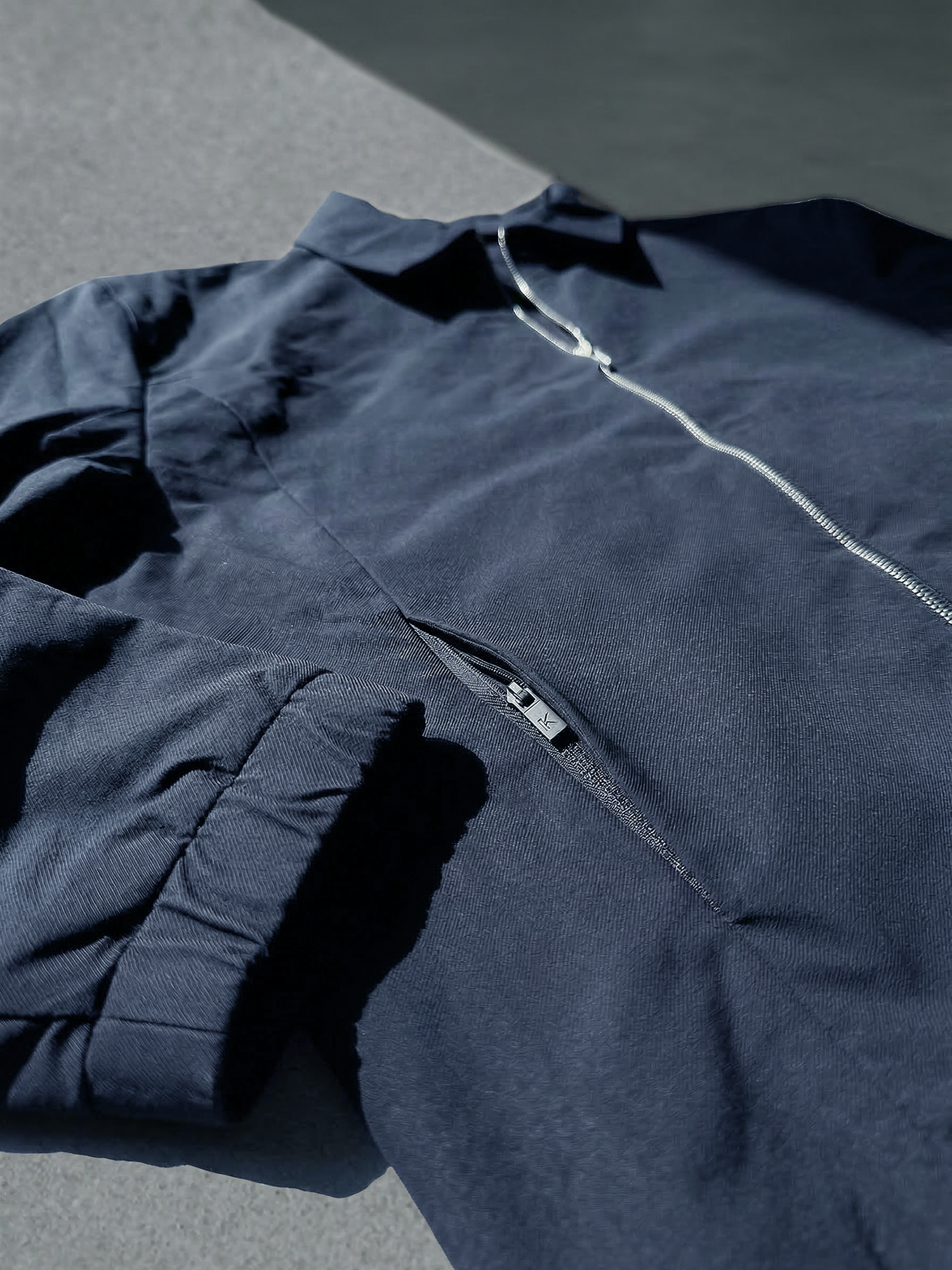 Détail d’une veste bleu marine avec fermeture éclair centrale et poche poitrine discrète.