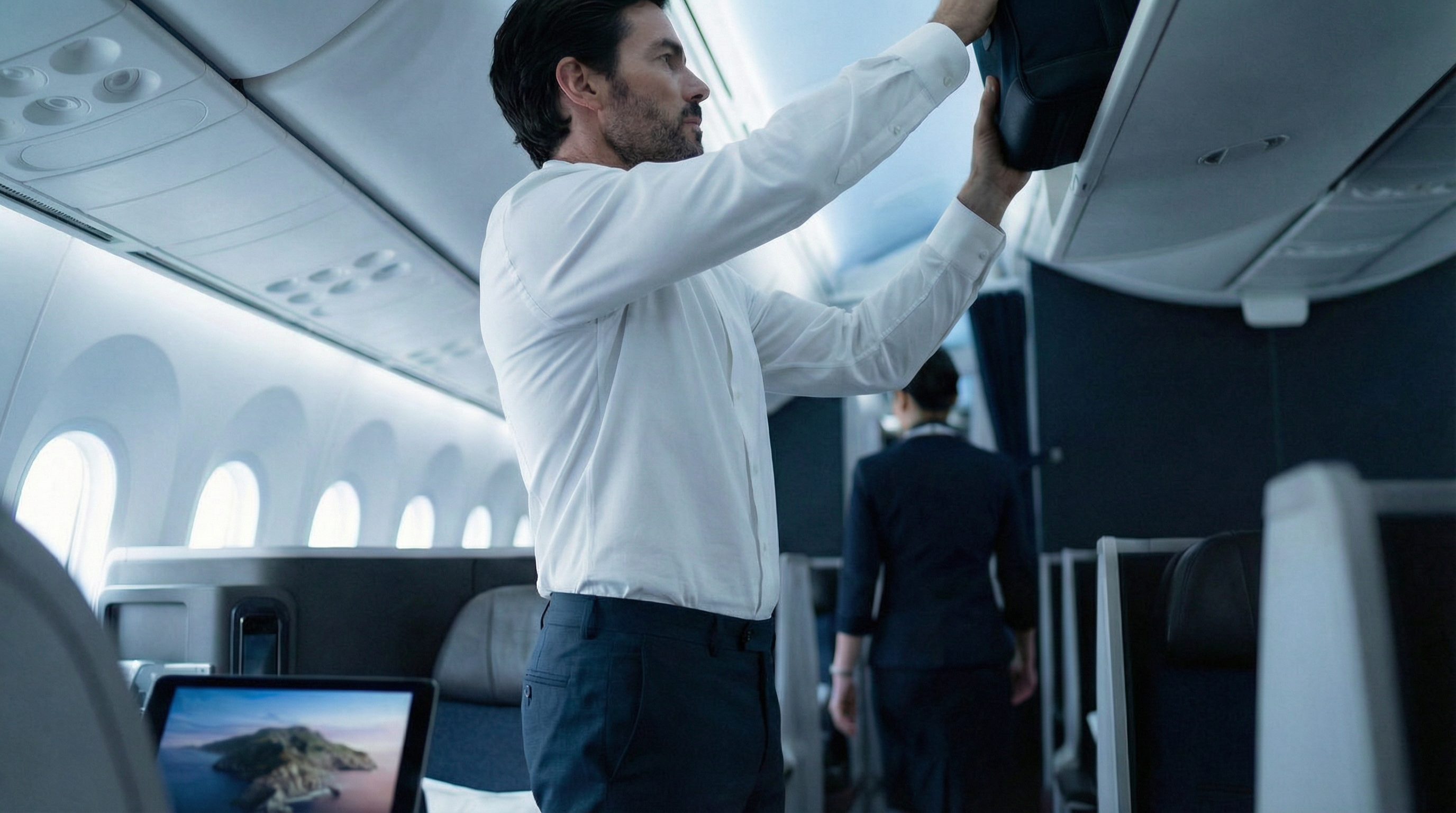 Homme en chemise blanche stretch col mao rangeant son sac dans un avion, coupe élégante et confortable.