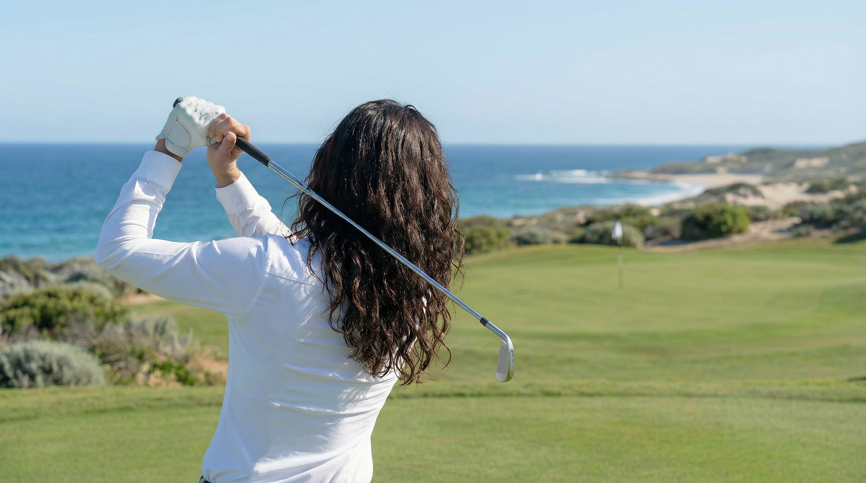 Femme portant une chemise blanche stretch lors d’une partie de golf en bord de mer.