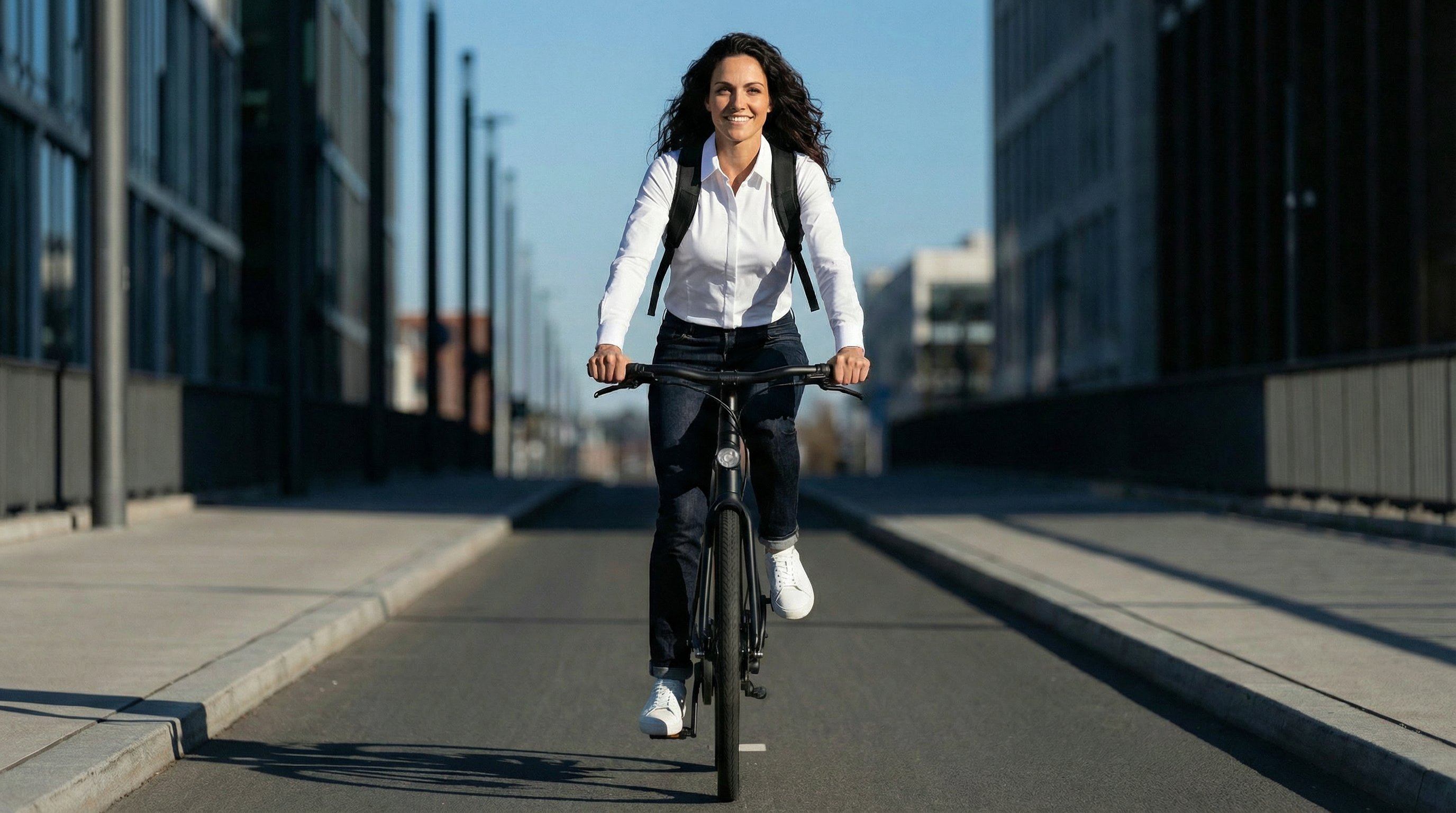 Femme portant une chemise blanche stretch à vélo dans un environnement urbain moderne.