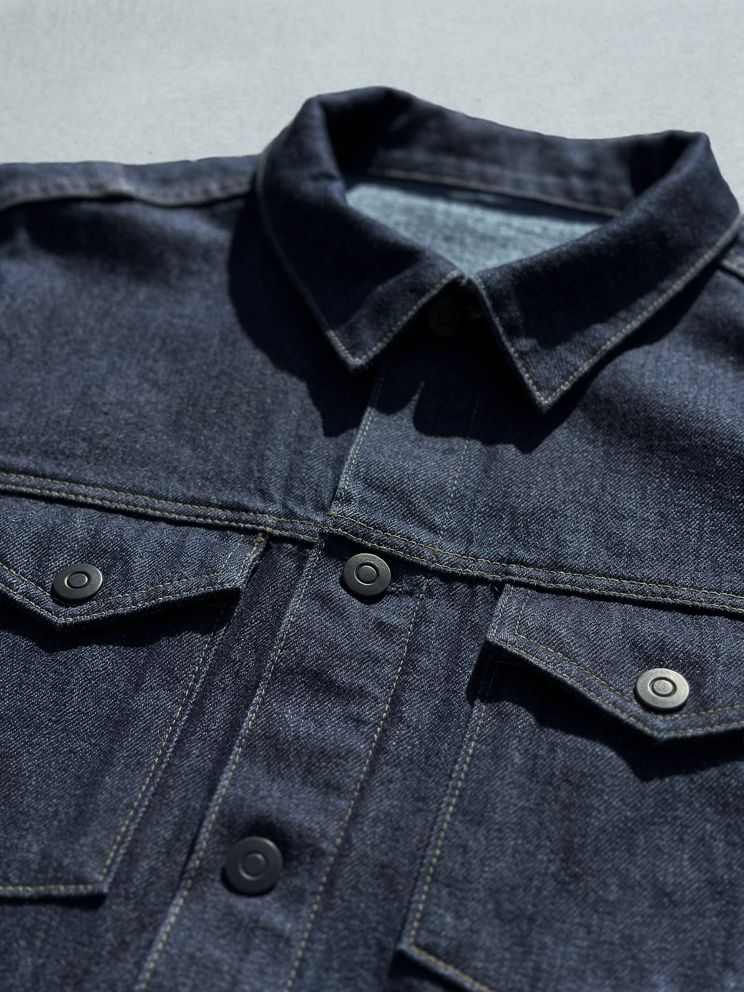 Détail du col et des poches poitrine d’une veste en jean bleu nuit avec surpiqûres contrastées.