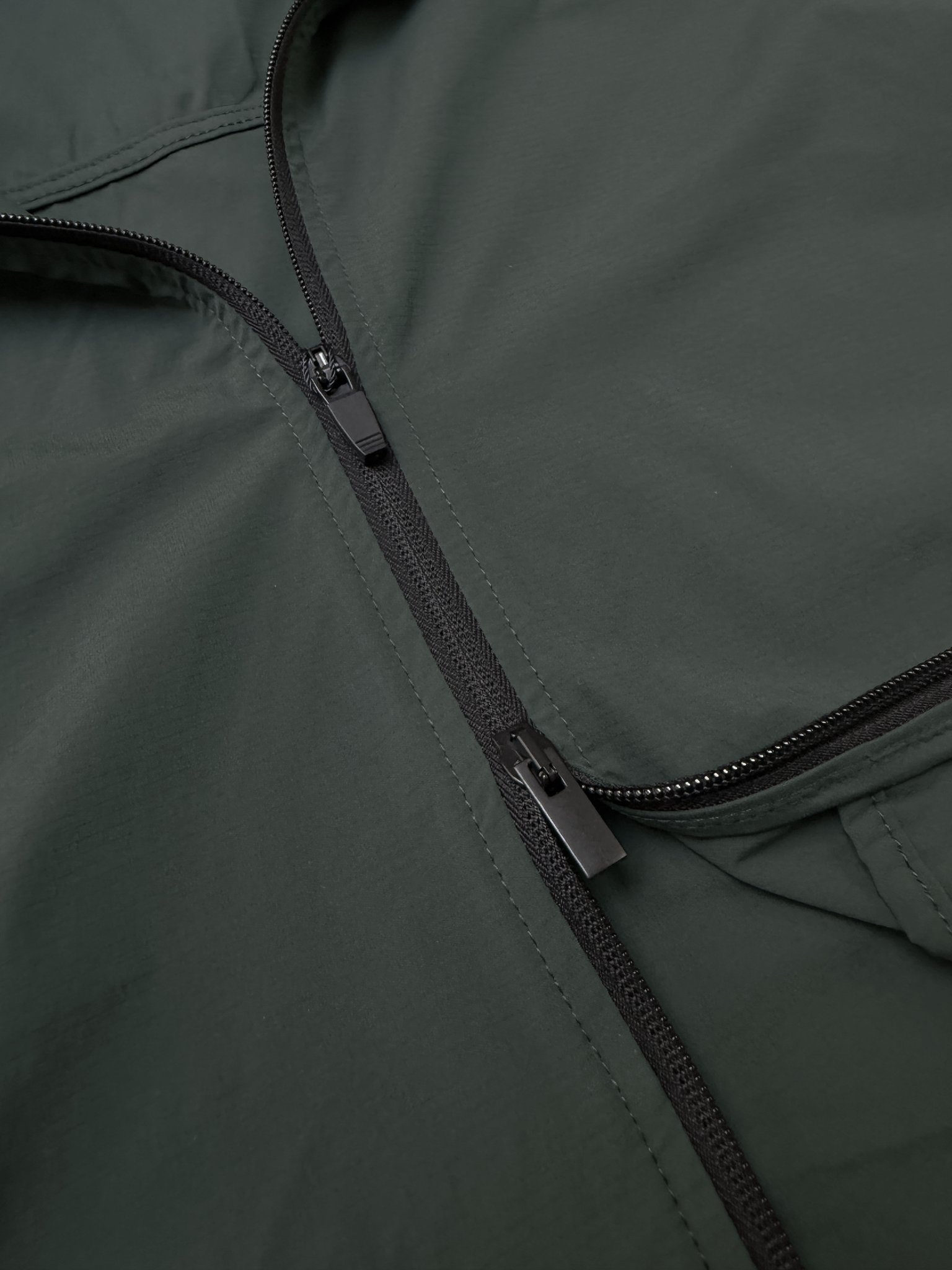 Gros plan sur fermetures éclair noires intégrées à une veste vert foncé minimaliste.