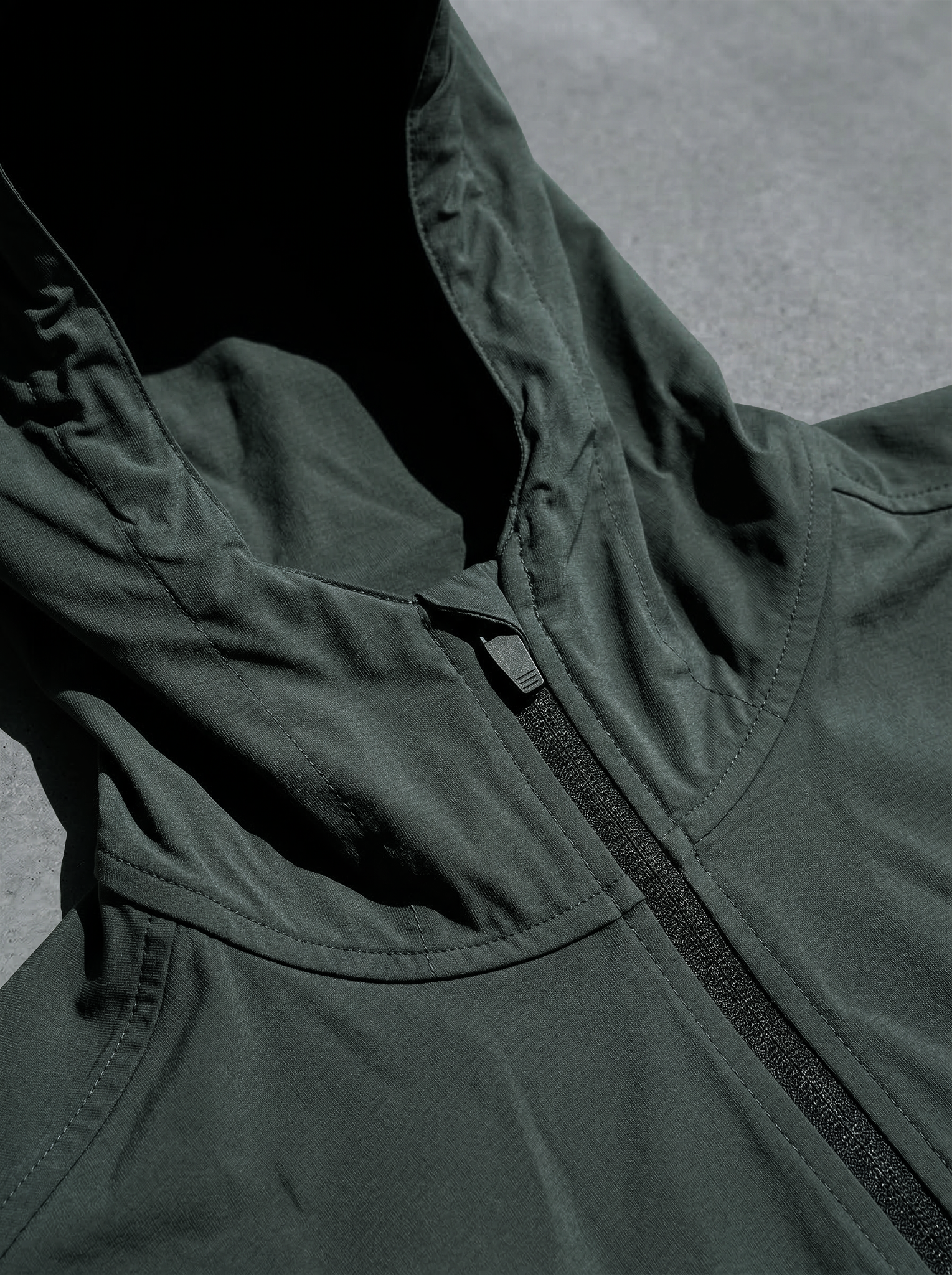 Gros plan sur capuche structurée et zip central noir sur textile vert foncé.
